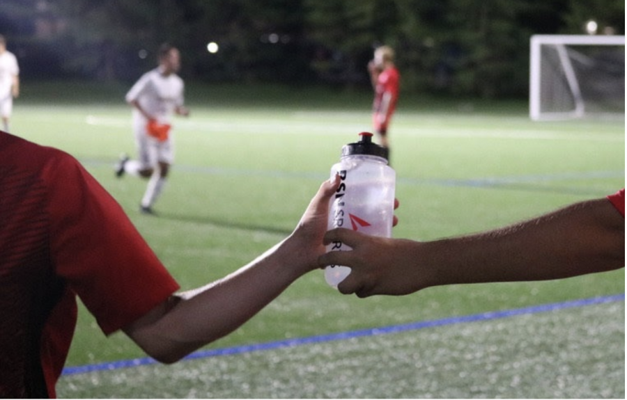 An athletic trainer hands off a water bottle to a player during a soccer match. Photo by G. Marsh