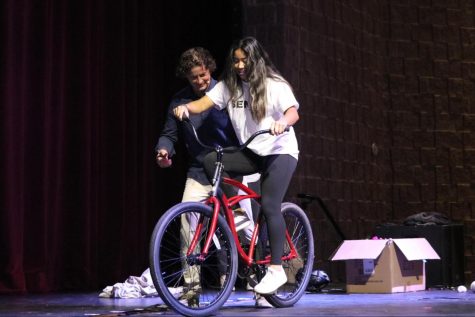 On the auditorium stage, senior Emmi Brown attempts to ride a reverse-steering bicycle for a Senior Seminar activity.