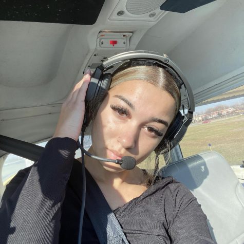 Wearing headphones, senior Kendyll Bigsbee poses for a photo in the cockpit of an airplane.