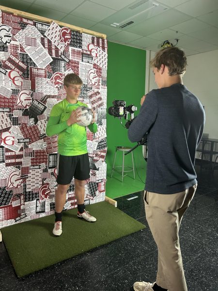 Junior Garrison Dowling takes a picture of sophomore Carter Dorrell during the boys soccer team's media day. Sports teams are brought in for different types of pictures that can be used on the Trojaneer Sports instagram, or an athletes personal social media. "I think the environment of media day was fun," Dorrell said. "Being there with all of my teammates helped make it fun for everyone involved. I think this is good for student athletes to experience, so they know how to be comfortable in front of a camera."