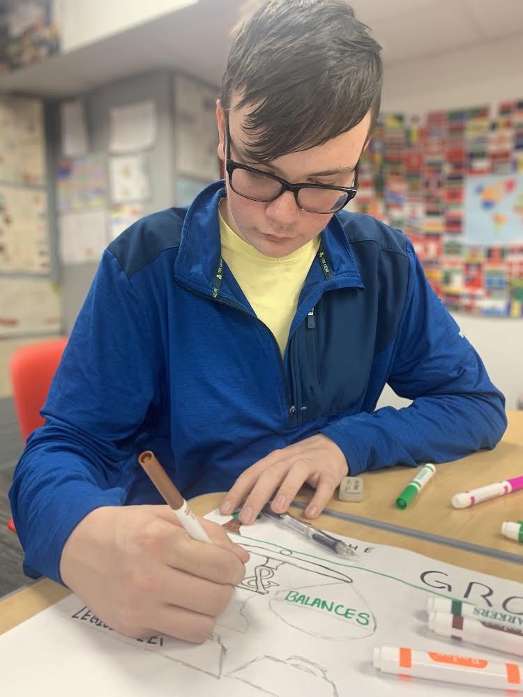 Junior Ryan Merrill colors in the picture representing “checks and balances” on his poster over the US Constitution in Josh Hart’s APUSH class. Students completed this poster activity to model the impacts that the ratification of the Constitution had. “We made the poster to discuss whether the US Constitution was groundbreaking article or if it was more of a flawed thing,” Merrill said. “I think this activity was useful for us to be able to dissect the impact that the Constitution had in our history.”