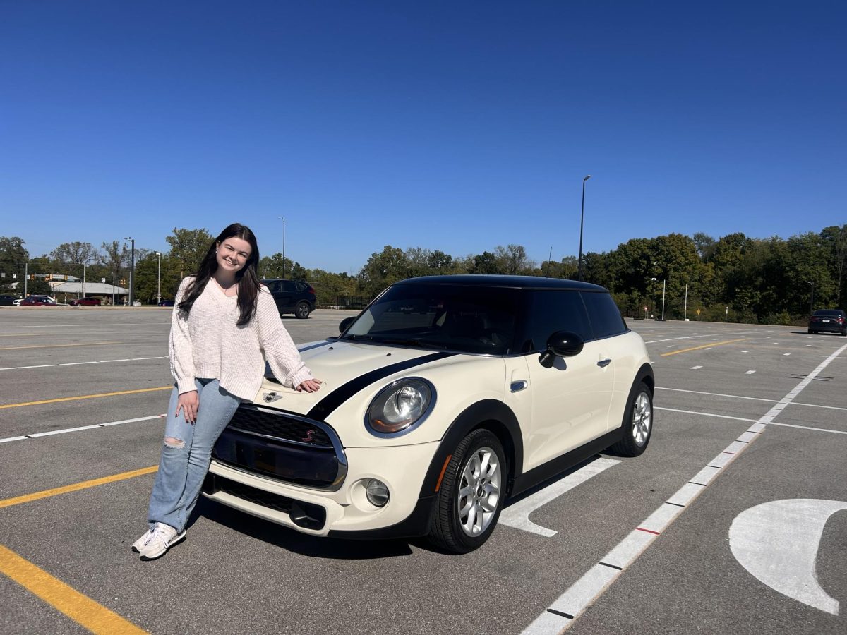 Junior Audrey Osborne poses in the school parking lot with her mini cooper that she refurbished with her dad.