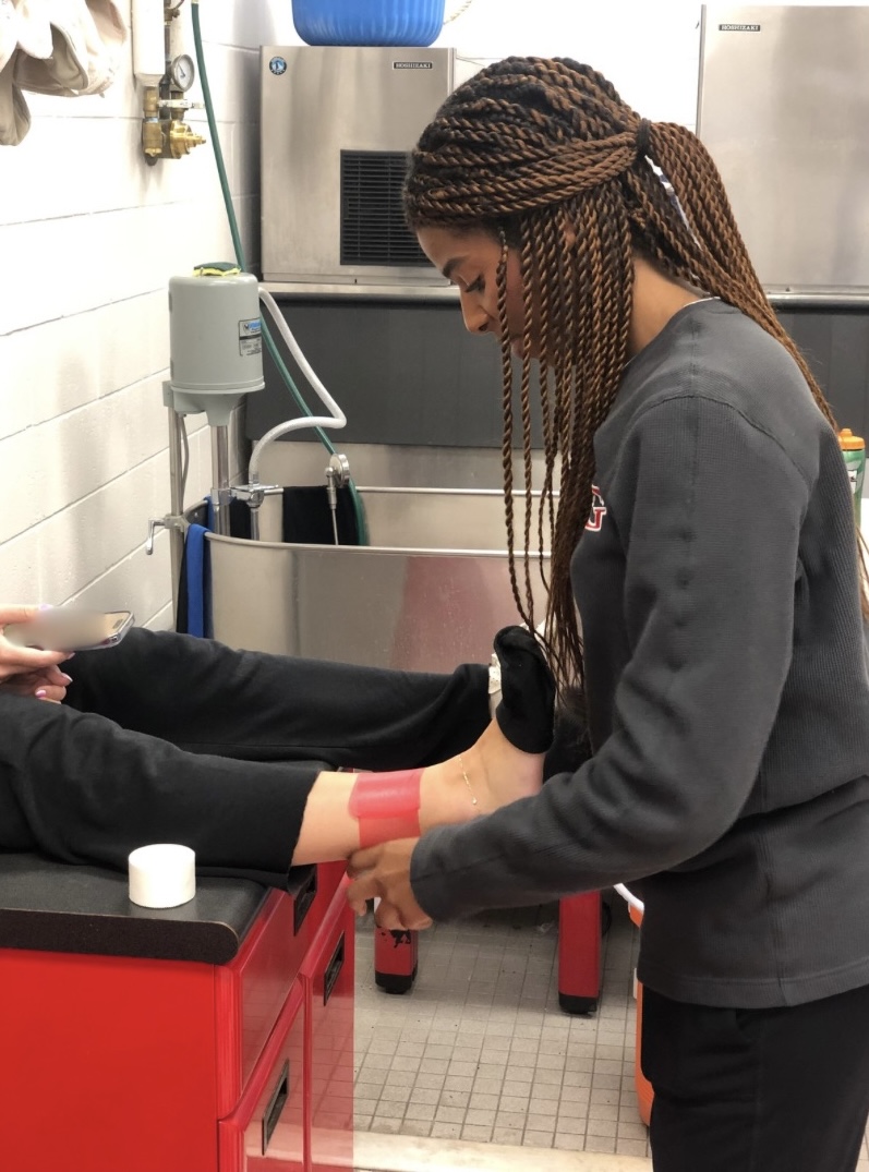 Head athletic trainer Azizi Chambers tapes an ankle in the outdoor locker room after school.