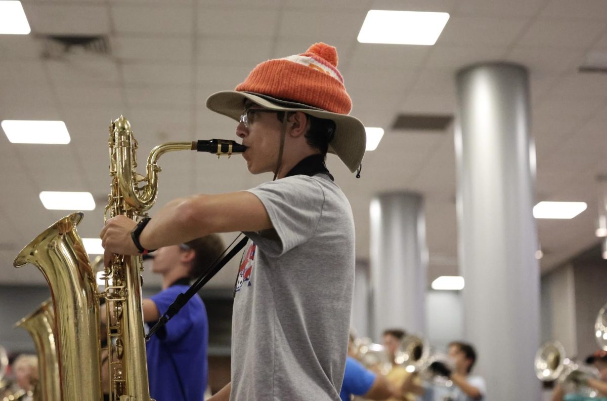 "Covered Practice | Sophomore Derek Groeper practices a segment of part three of the marching show in the cafeteria. On Tuesday the marching band was forced inside due to a downpour which affected the last part of their practice. ""We try to keep relatively the same playing level as we do when we're outside,"" Groeper said. ""When we're outside and doing drill it's a lot harder to listen to people on the other half of the field compared to when we are inside the sound echoes around.”