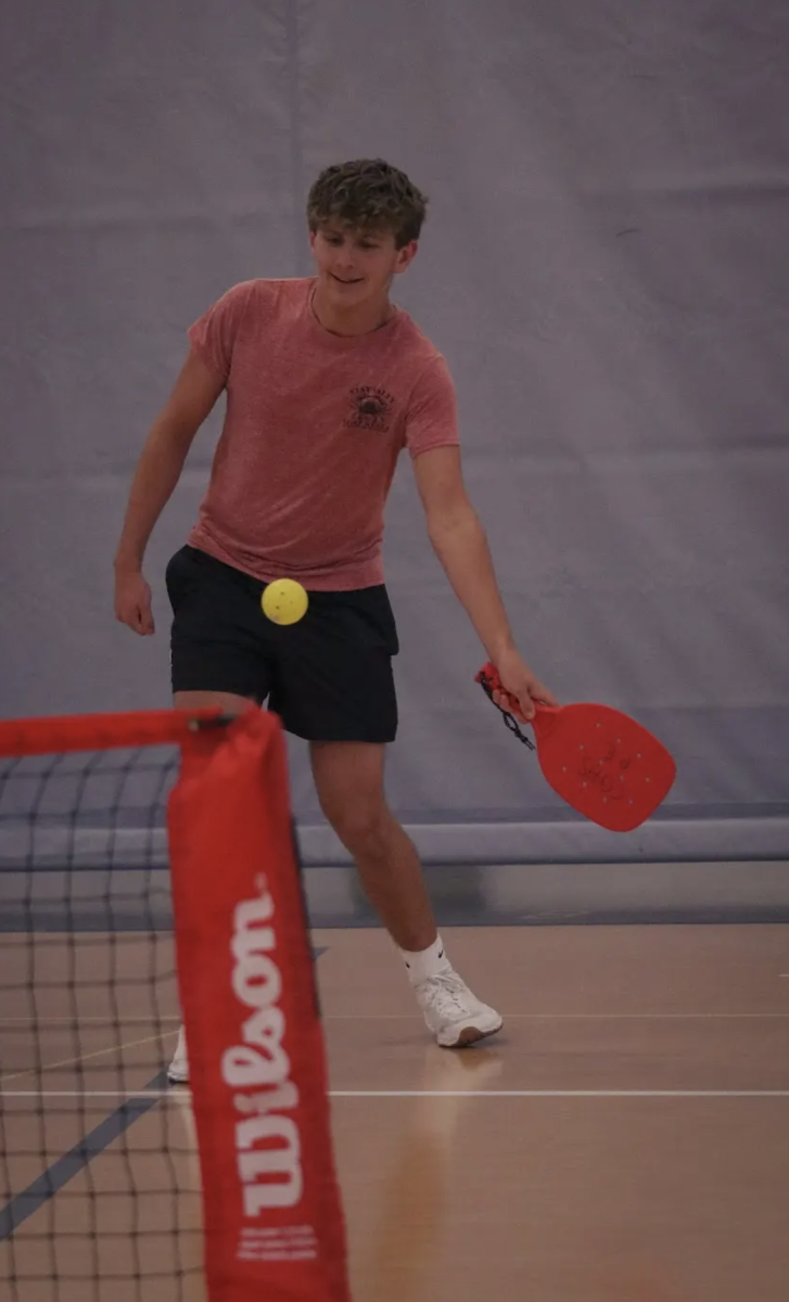 Sophomore Aiden Wogoman hits a pickleball over a net in the SAC during a routine pickleball club meeting. Wogoman helped to found Pickleball Club with the goal of bringing the sport to its full potential within the school. “We started the club fair this year and put posters up around the school and I do expect it to grow more in the future,” Wogoman said, “I would encourage others to join because you can play with your friends right after school and it’s easier to get together.” Pickleball club meets every other Wednesday in the Hall of Excellence.