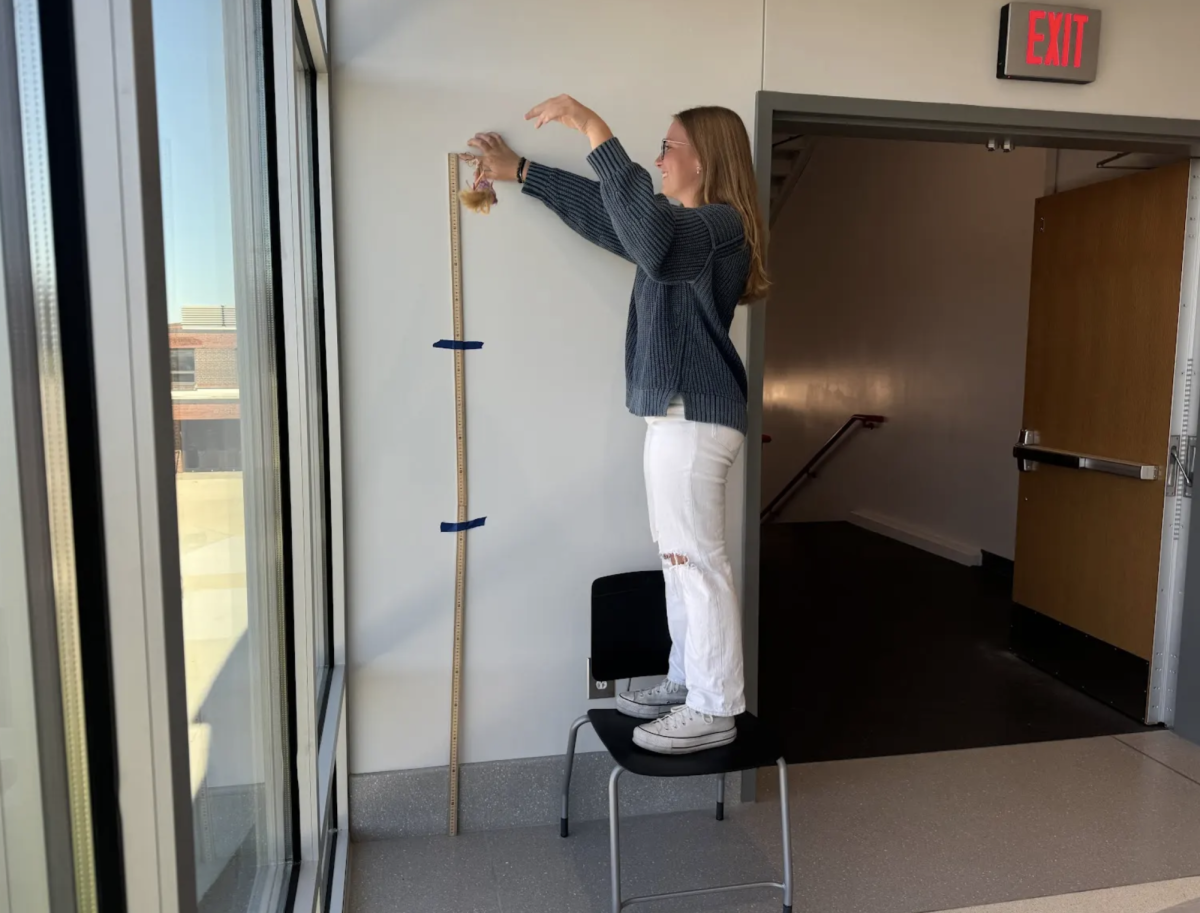 "Senior Emma Barton prepares to drop a rubber band-covered Barbie doll in Julie Coyne’s 4th period AP Statistics class. The goal of the activity was to use a least squares regression line to predict the amount of rubber bands needed to drop a Barbie off a ledge without the doll’s head hitting the floor, and Barton’s group was the class winner, as the doll got the closest to the ground without making contact. “I thought that the way we ran the experiment strongly contributed to our group’s win,”  Barton said. “We made sure that each time we tested, we dropped our Barbie from the exact same place and had a camera to show exactly where she reached the lowest point. The best part of this activity was all the laughter that came along with it. It was a completely ridiculous scenario to test, and every time our Barbie hit the wall, our group would erupt in laughter.”