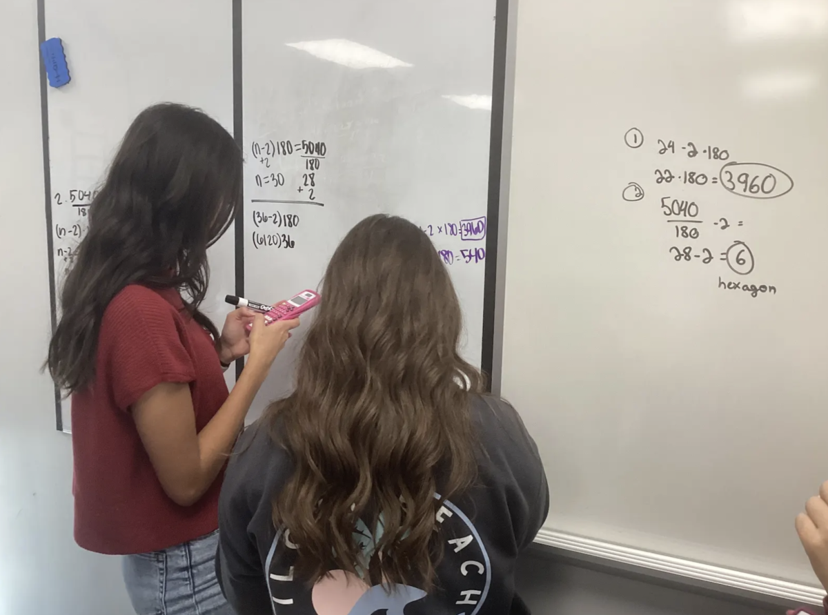 Juniors Maya Emerson and Izzy Blanchard work on the white boards in Geometry class to solve problems. “Going to the whiteboards allows us to collaborate with our partners and work together to help each other out,” Blanchard said. 