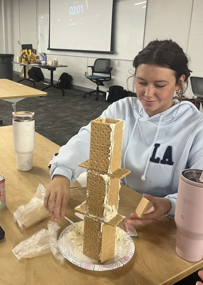 "In an attempt to make the largest gingerbread house at the Science NHS meeting, Junior Elle Justice adds the finishing touches as the timer runs out. Her team’s careful planning and steady hands helped keep the towering gingerbread house standing. “We used a wide base along with tall rectangular walls to give it stability and height to pull off the win,"" Justice said. Justice and her group were able to pull off the win after 10 minutes of building."