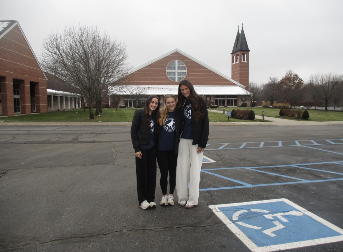 Juniors Charley Harpe, Samantha Thomas, and Ella Wolfe pose in front of Saints Francis and Clare of Assisi Church.