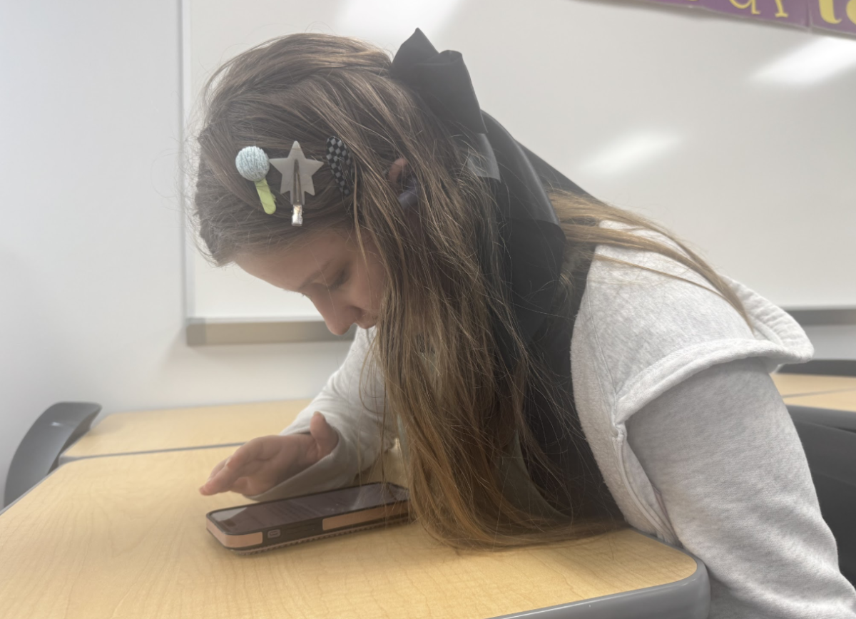Peering over her phone in study hall, Kiara prepares to write a tumblr story for her blog.
